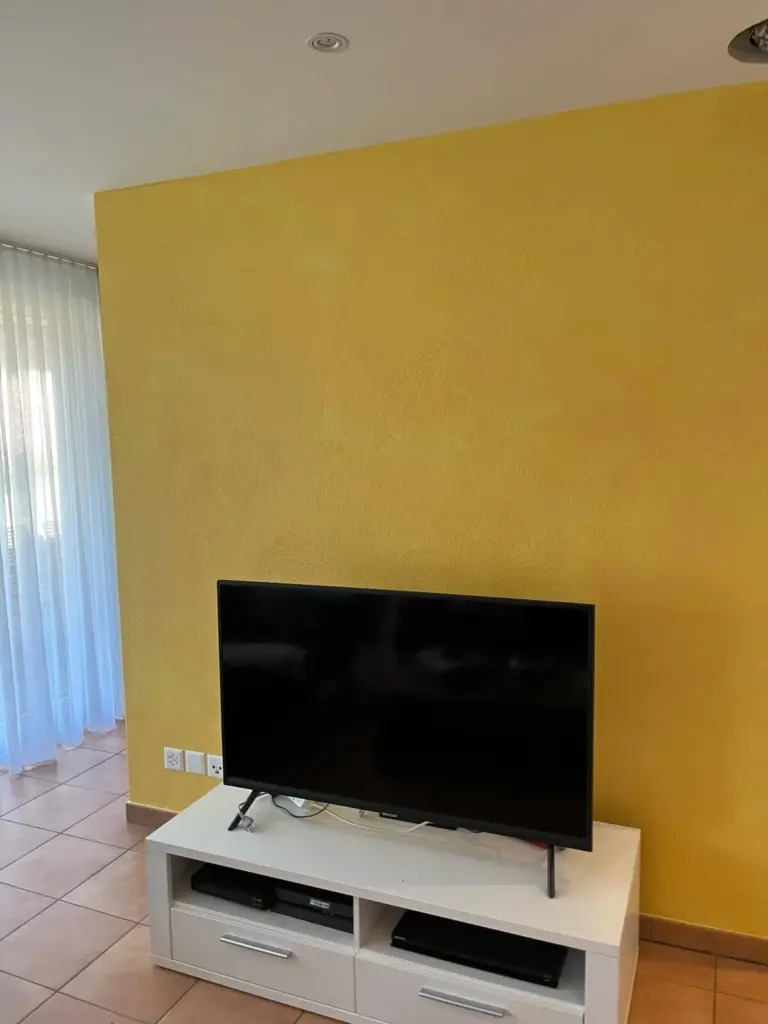 Wohnzimmer mit ockergelber Akzentwand hinter dem Fernseher