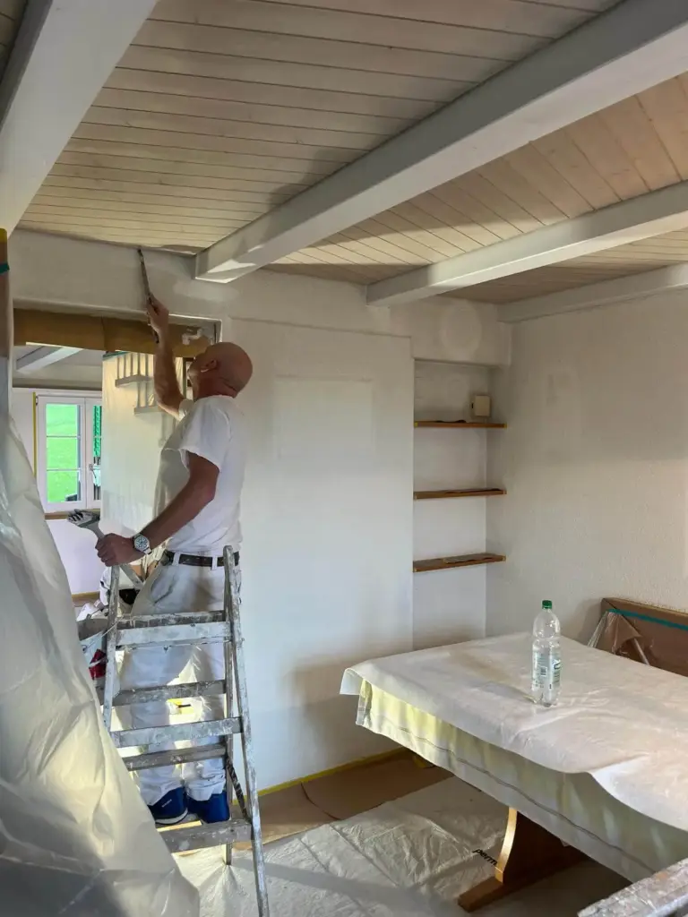 Maler streicht auf der Leiter die Decke eines Wohnraums
