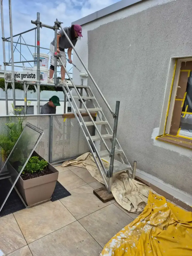 Zwei Mitarbeitende streichen eine Fassade vom Gerüst aus