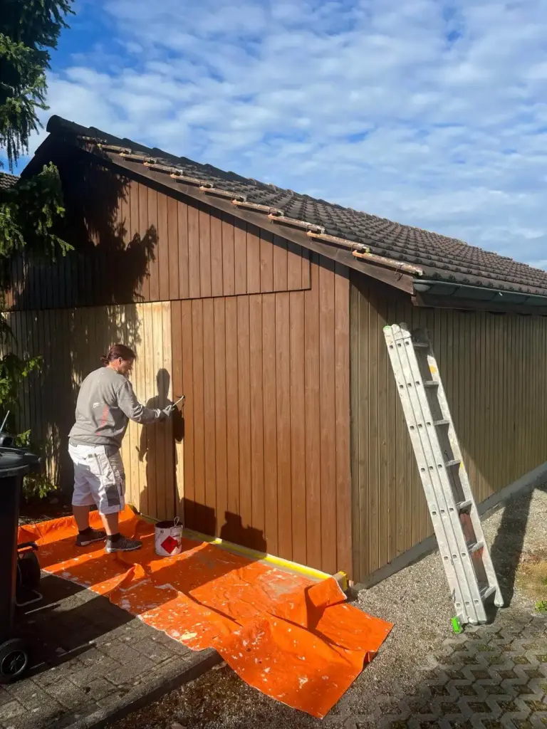 Mitarbeiterin lasiert die Holzfassade einer Garage