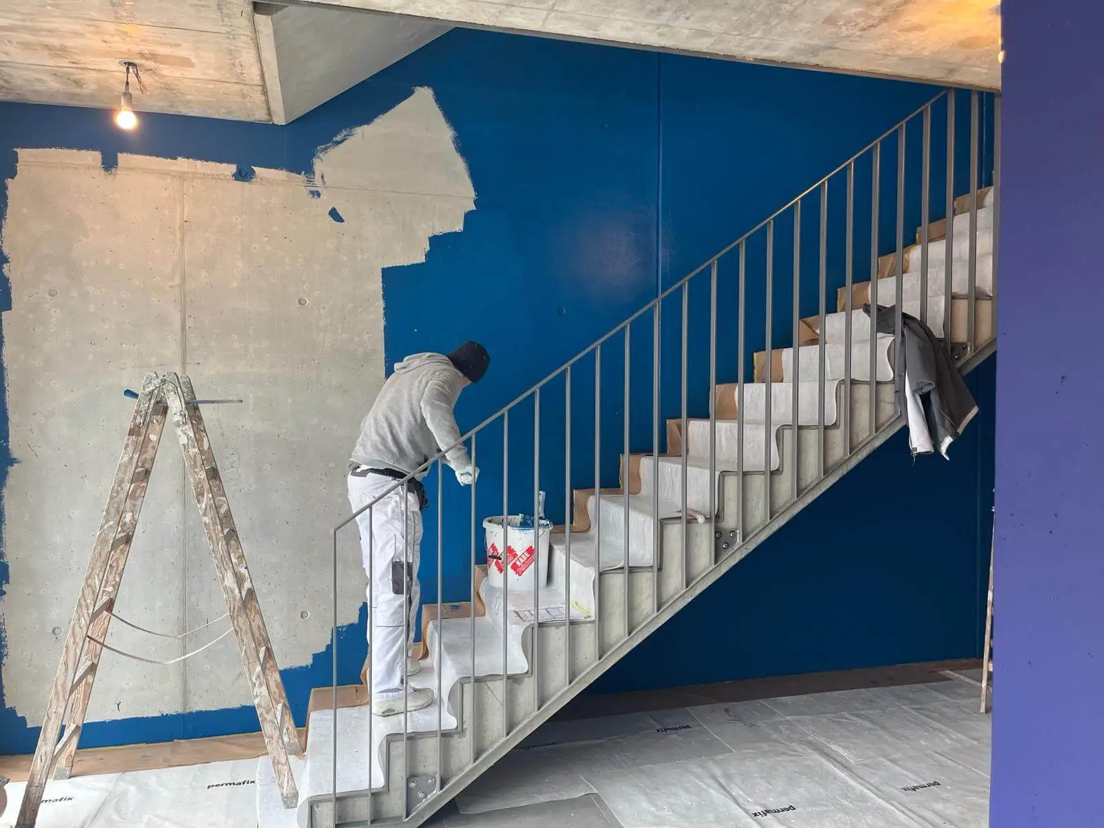 Maler streicht die Wand eines Treppenhauses in kräftigem Blau