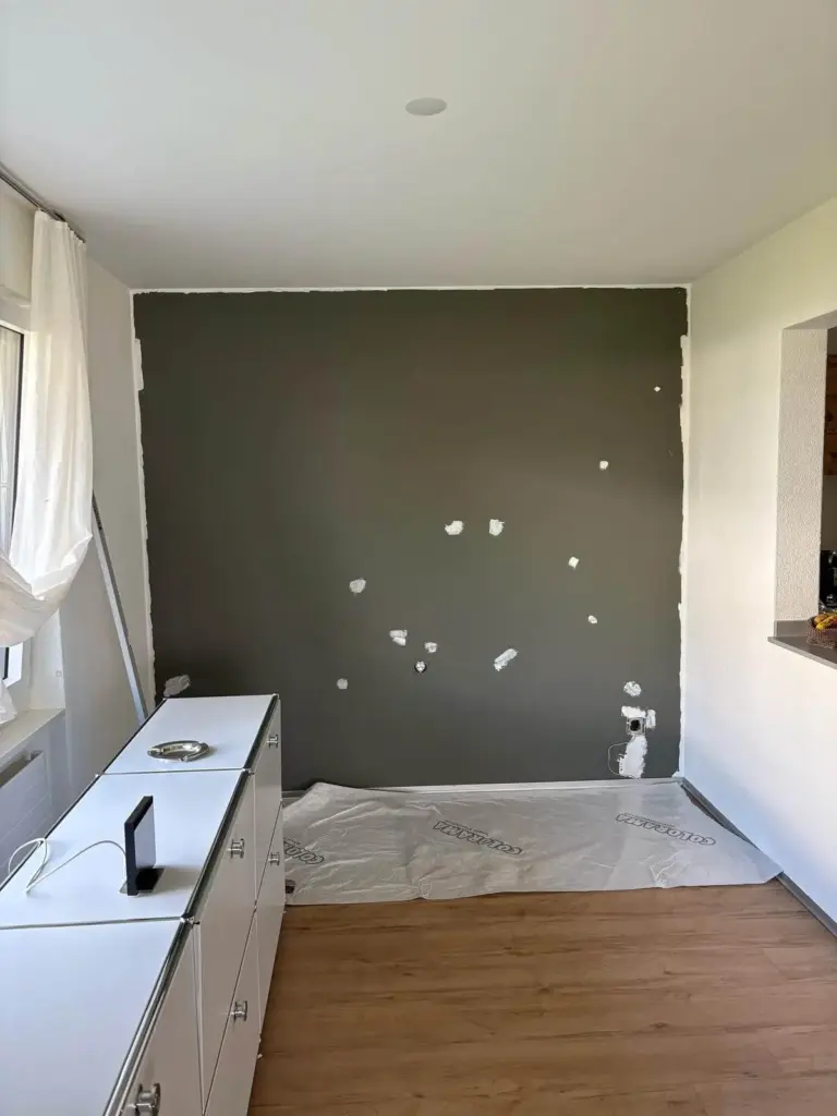 Dunkel gestrichene Wand mit gespachtelten Bohrlöchern vor der Neugestaltung