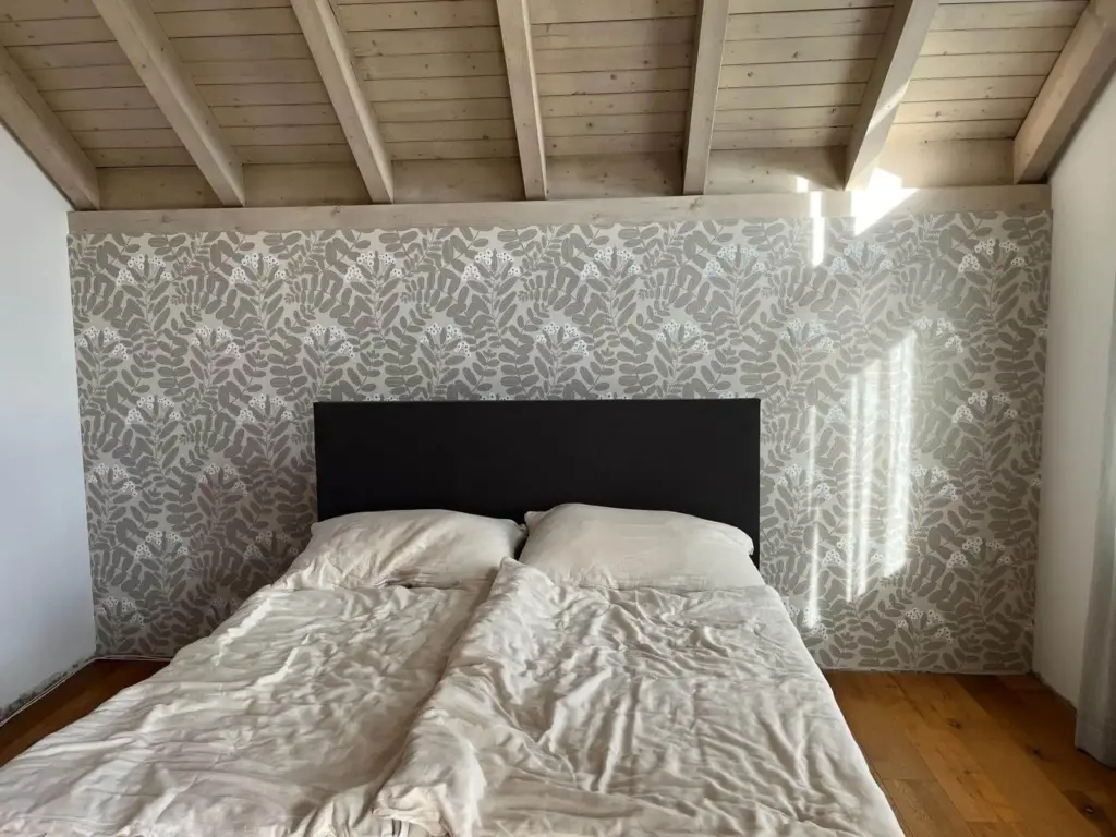 Schlafzimmer unter dem Dach mit floral gemusterter Tapete hinter dem Bett